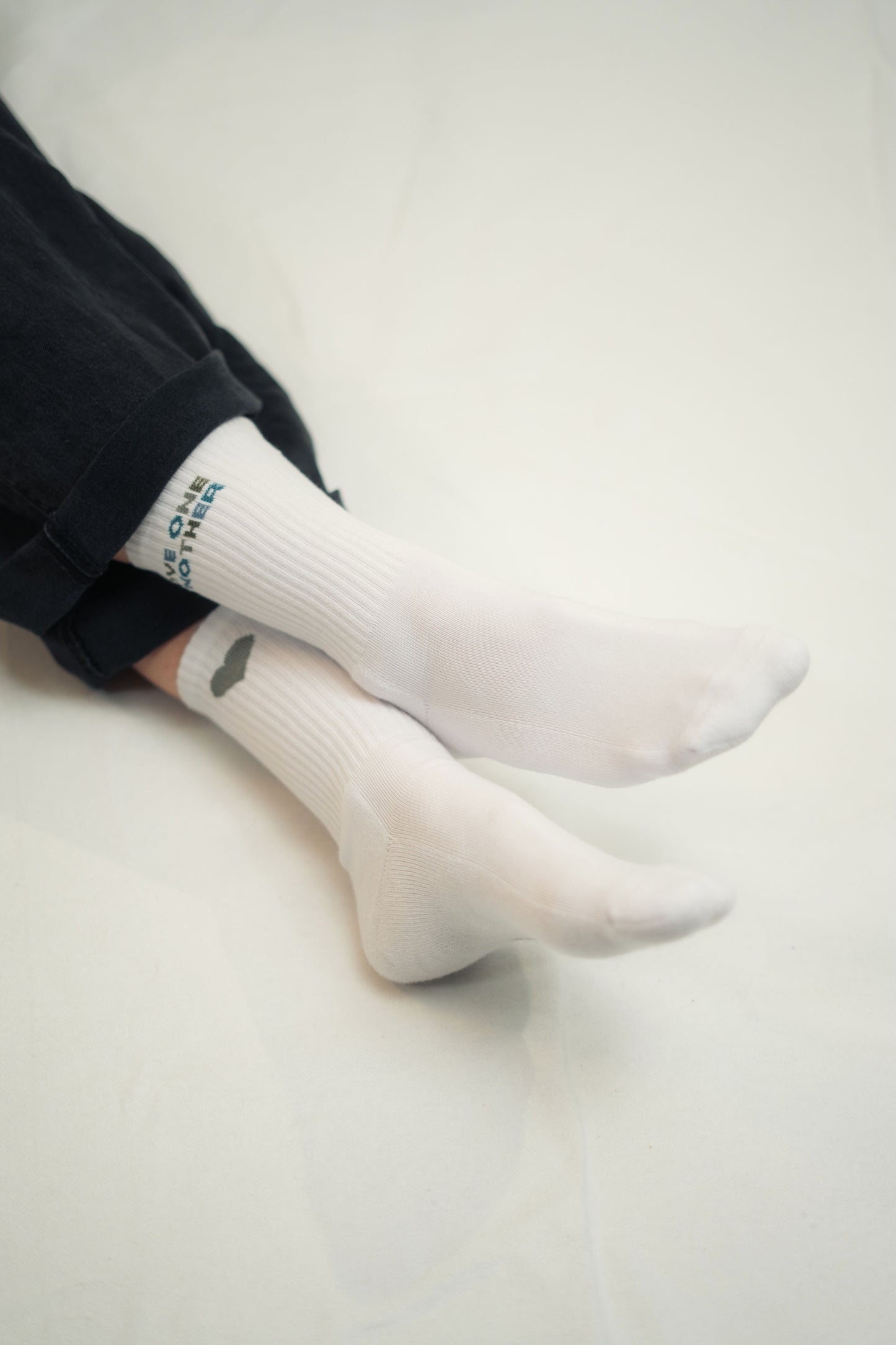 Model trägt Mission One More weiße Socken aus Baumwolle und zertifizierter Herstellung mit Glaubensbezug "Love One Another"