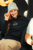 Model sitzt entspannt im Wohnzimmer mit Mission One More Organic Shirt & Beanie Faith Inspired Fashion