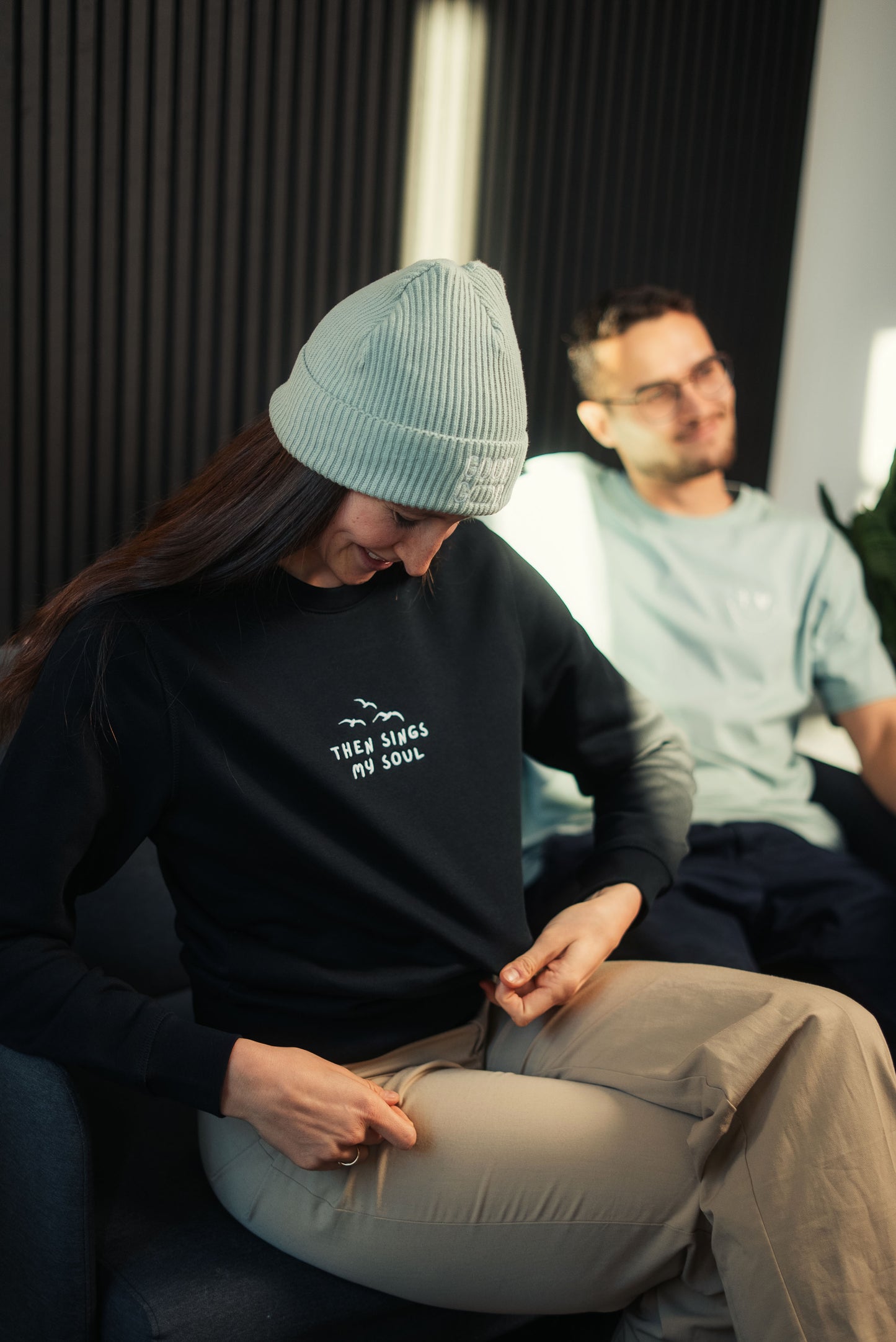 Model mit Mission One More Faith Sweatshirt entspannt in Sofa-Setting nachhaltige & faire Marke