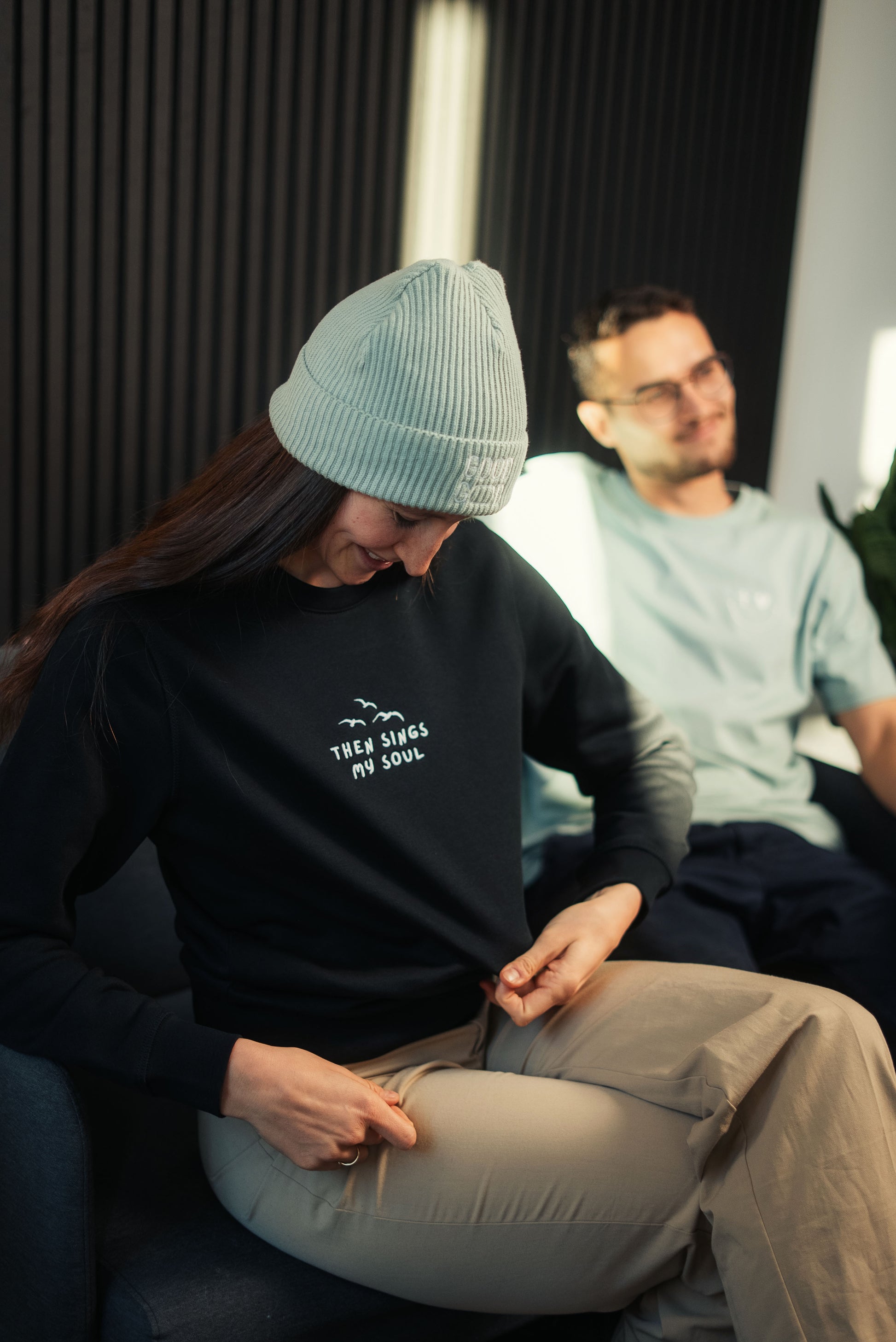Model mit Mission One More Faith Sweatshirt entspannt in Sofa-Setting nachhaltige & faire Marke
